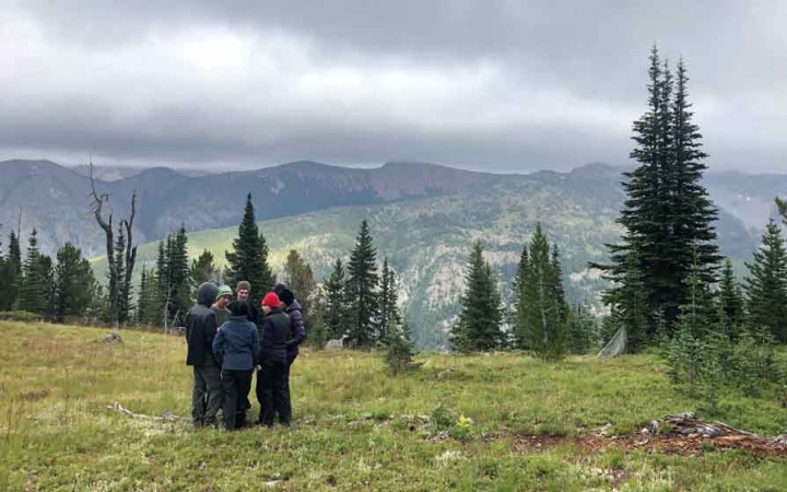 a group of students stand in a mountain meadow with a mountainous landscape in the background